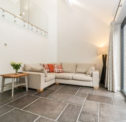 A living room with a beige sectional sofa a wooden side table with flowers floor lamp and sliding glass doors at Willow Barn in Shapwick