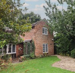 A brick house with white windows surrounded by trees and a garden with grass and gravel at The Coach House Apartment in Bredon