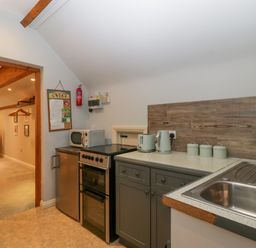 A kitchen with a stove refrigerator microwave kettle toaster and sink next to a living area with a television and dresser at The Coach House Apartment in Bredon