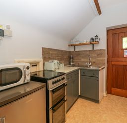 A kitchen with a microwave on a fridge next to an oven a sink with a faucet wooden door and shelves with glasses at The Coach House Apartment in Bredon