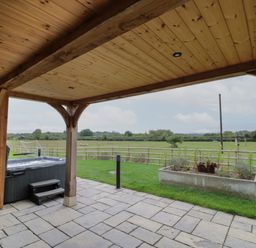 A covered patio with a hot tub and a planter overlooking a fenced grassy field at Hallgarth Farm Holiday Lodge in Peopleton