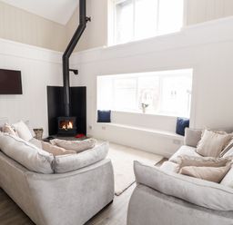 A living room with two sofas a wood burning stove and a window seat with cushions at Sgubor in Valley