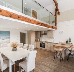 A kitchen and dining area with a white table and chairs and a wooden countertop with stools at Sgubor in Valley