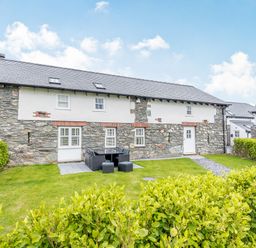 A stone and white exterior house with green lawn outdoor seating and hedges at Sgubor in Valley