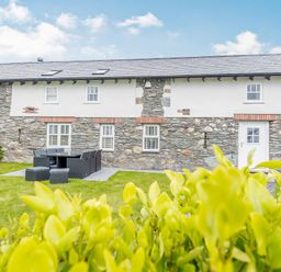 A stone and white exterior house with a patio dining set on a grass lawn at Sgubor in Valley