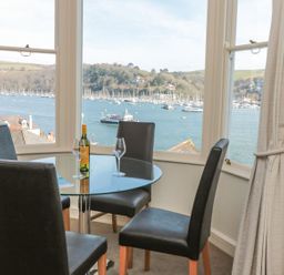 A dining area with a round glass table and four chairs overlooking a harbor with boats at 4 Dartview in Dartmouth