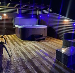 An outdoor hot tub on a wooden deck with wicker chairs and a table at Redwood Retallack in Retallack near St Columb Major