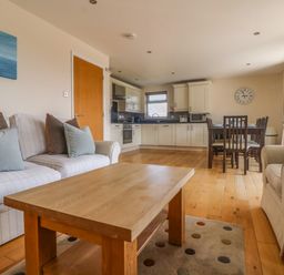 An open-plan living room with sofas a wooden coffee table kitchen cabinets and a dining table with chairs at Redwood Retallack in Retallack near St Columb Major