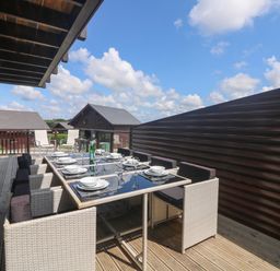 An outdoor dining area with table set for eight and chairs on a wooden deck at Redwood Retallack in Retallack near St Columb Major