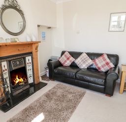 A living room with a fireplace a black leather sofa with cushions a wooden side table and a rug at The Nook in Benllech