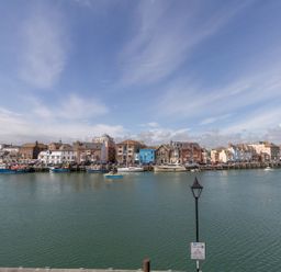 A harbor with boats docked along the waterfront and buildings in the background at Harbourside Cottage in Brewers Quay Harbour