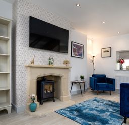 A living room with a fireplace a television blue chairs and a blue rug at The Old Sweet Shop in Conwy