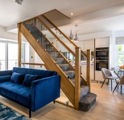 An open living space with a blue sofa near carpeted stairs and a kitchen dining area with a glass table and chairs at The Old Sweet Shop in Conwy