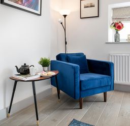 A blue armchair next to a wooden side table with a teapot cup plant and plate of pastries at The Old Sweet Shop in Conwy