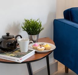 A side table with a black teapot white mug a book potted plant and a plate of pastries next to a blue sofa at The Old Sweet Shop in Conwy