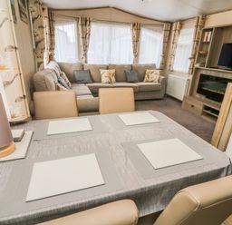A dining table with placemats and a lamp in front of a sofa and a television in a living area at 12A Borwick Lakes South Lakeland Leisure Village