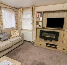 A living room with a sofa curtains and a TV on a wooden unit with an electric fireplace at 12A Borwick Lakes South Lakeland Leisure Village
