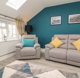 A sitting room with gray armchair and sofa with cushions near a window and teal painted wall with framed pictures at New Inn Apartment in Tholthorpe near Easingwold