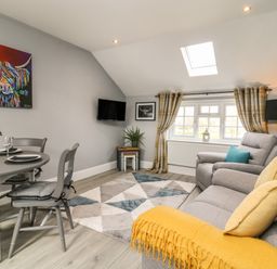 A living room with a gray dining table and chairs a colorful painting and a gray sofa with yellow cushions at New Inn Apartment in Tholthorpe near Easingwold