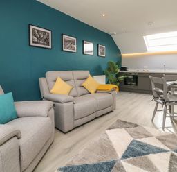 A living room with gray sofas and yellow and blue cushions near a kitchen and dining table at New Inn Apartment in Tholthorpe near Easingwold
