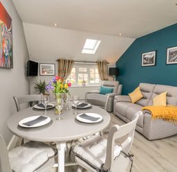 A dining table with four place settings and a vase of flowers in a living room with sofas and cushions at New Inn Apartment in Tholthorpe near Easingwold