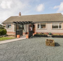 A bungalow with a gravel driveway a black pergola and garden beds at The Croft Bungalow in Plumbland near Aspatria