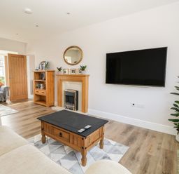 A living room with wooden furniture a wall-mounted TV a fireplace and a potted plant at The Croft Bungalow Plumbland near Aspatria