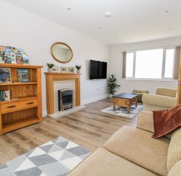 A living room with a beige sofa and armchair wooden bookshelf wooden coffee table fireplace and wall-mounted TV at The Croft Bungalow in Plumbland near Aspatria