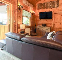 A living room with a brown leather sofa and a wooden cabinet with a wall mounted television at Gisburn Forest Lodge Tosside near Wigglesworth