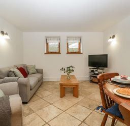 A living room with beige tiled floor sofa coffee table tv and dining table with croissant at Bluebell Cottage in Pembridge