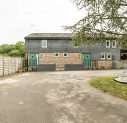 A driveway with a two door stone and wood exterior building and a tree with a round metal bench at Bluebell Cottage in Pembridge