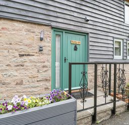 A green door with a sign bluebell cottage on a stone and wood house exterior with flower boxes and a black iron railing at Bluebell Cottage in Pembridge