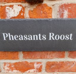A black slate house name sign on a red brick wall with the text Pheasants Roost at Pheasant's Roost in Lelley near Burton Pidsea