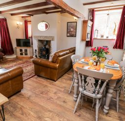 A living and dining area with brown leather sofas a wooden dining table set with breakfast and a fireplace at The Lodge in Stainsacre near Whitby