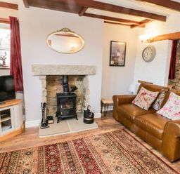 A living room with leather sofa and floral cushions fireplace and TV on a cabinet at The Lodge in Stainsacre near Whitby