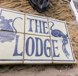 A sign made of tiles with the words The Lodge and drawings of two mice on a stone wall at The Lodge in Stainsacre near Whitby