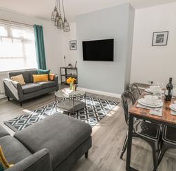 A living room with grey sofas a dining table set with plates and glasses and a wall mounted TV at Pebble Cove in Amble