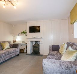 A living room with two grey sofas with green cushions a fireplace with a wood stove and a TV mounted above at Apple Barn in Crantock