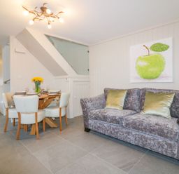 A dining area with a wooden table set for four and a sofa with cushions under a painting of a green apple at Apple Barn in Crantock