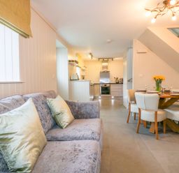A living room with a sofa and cushions opening to a kitchen and dining area with a table set for four at Apple Barn in Crantock