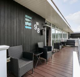 A wooden porch with black wicker chairs and a small table outside a building with dark walls at 98 Cherry Park in Chapel St Leonards
