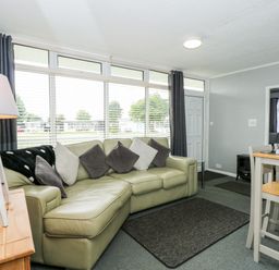 A living room with a leather sofa and pillows a wooden lamp table and a dining table with chairs at 98 Cherry Park in Chapel St Leonards