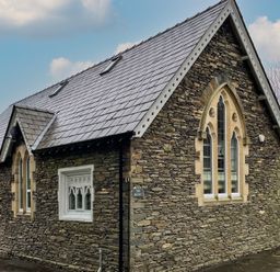 A stone building with arched windows and a gray tiled roof at The Belfry in Windermere