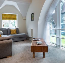 A sitting area with a grey sofa wooden coffee table and large arched windows at The Belfry in Windermere