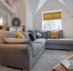 A living room with a gray sectional sofa and yellow cushions by a window with a yellow blind at The Belfry in Windermere