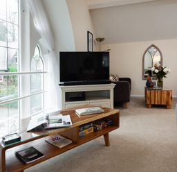 A living room with a wooden coffee table magazines a tv on a stand and a yellow armchair at The Belfry in Windermere