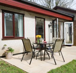 Outdoor patio with a glass table and four chairs near doors and windows of a house at Miles Retreat in Hayle