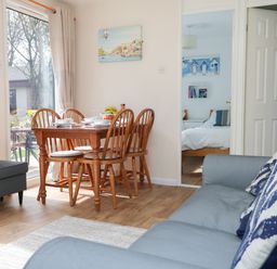 A dining area with wooden table and chairs next to a gray sofa and an open door showing a bedroom at Miles Retreat in Hayle