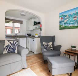 A living room with a gray armchair and ottoman next to nesting tables and a kitchen visible through an arch at Miles Retreat in Hayle