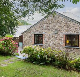 A stone cottage with two windows and flower bushes in front at The Roundhouse in Warbstow